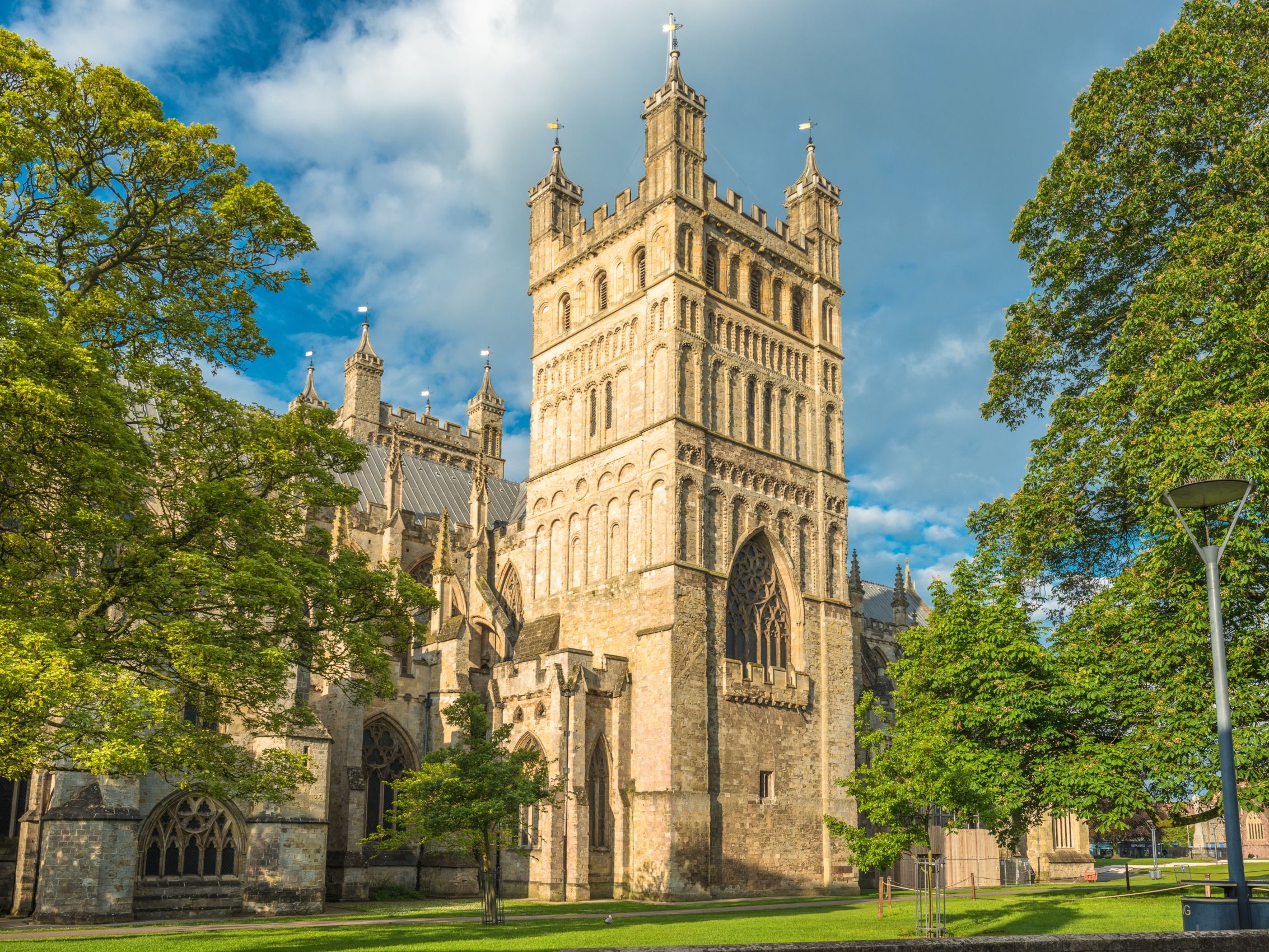 Stone cathedral tower framed by green trees under a blue sky