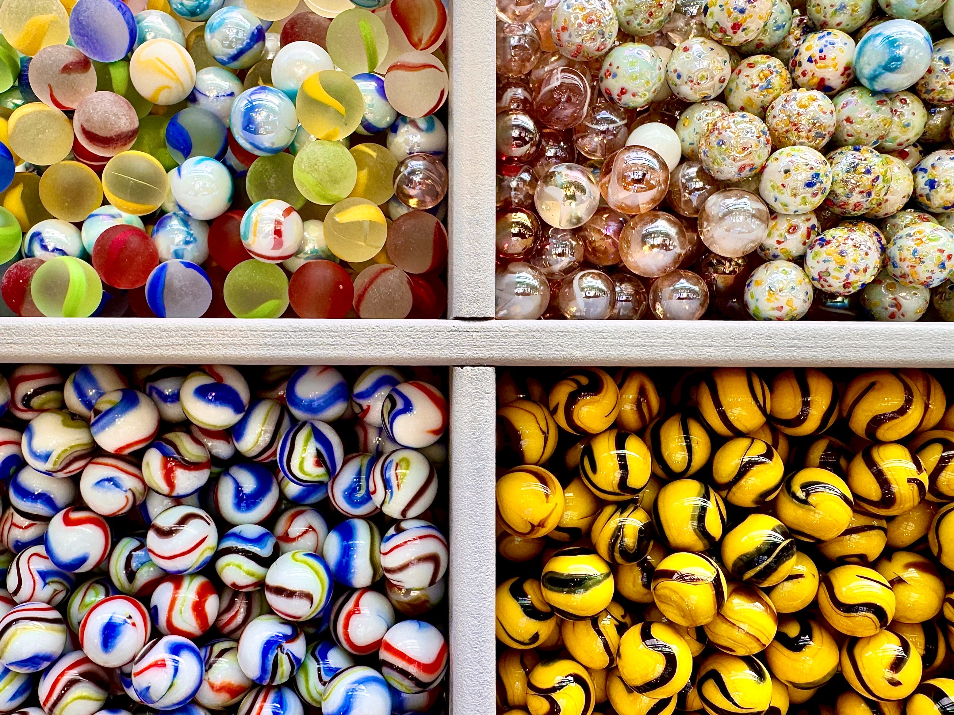 Four compartments filled with colourful glass marbles in a white tray