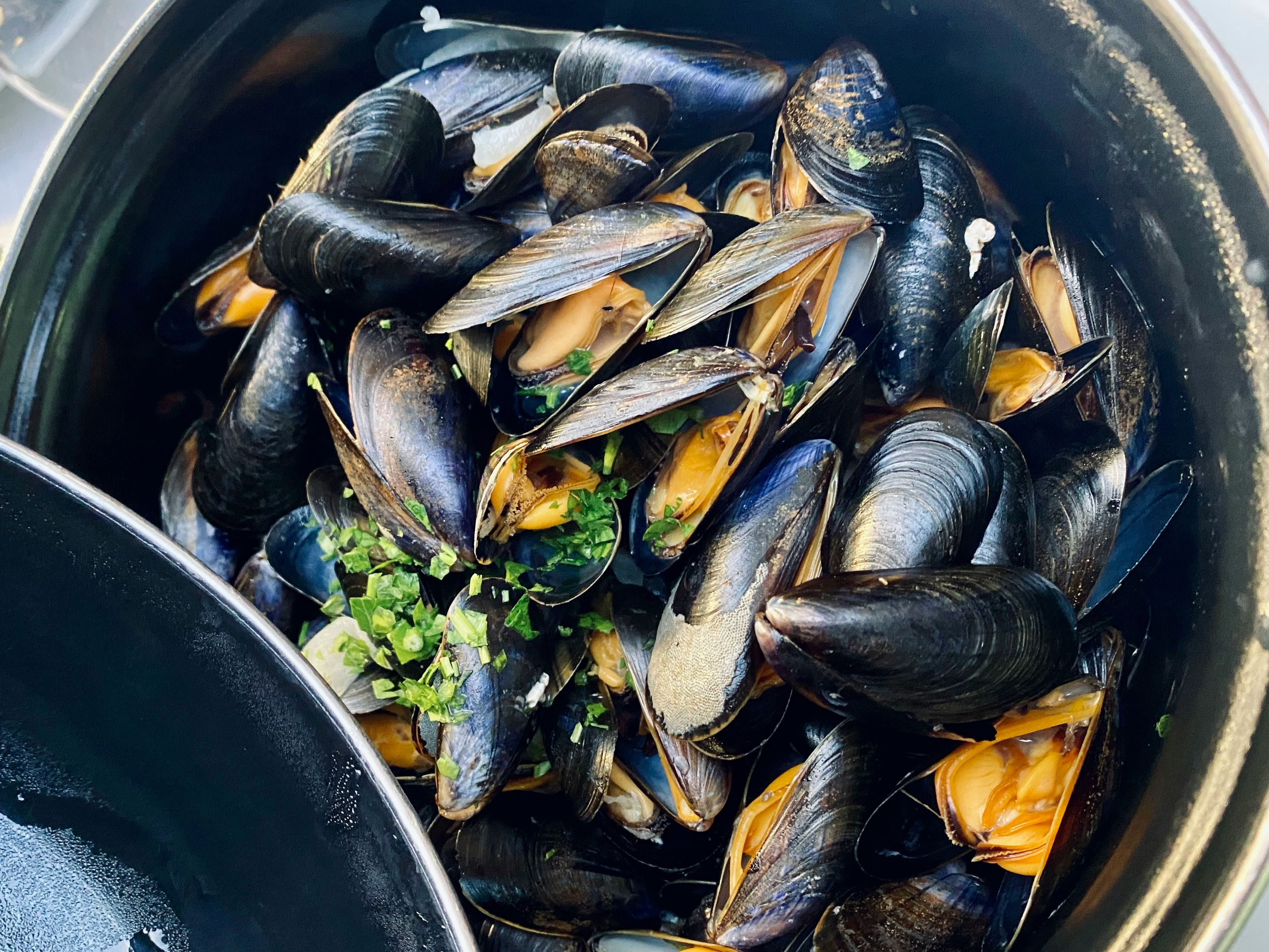 Steamed mussels in a black pot garnished with chopped herbs