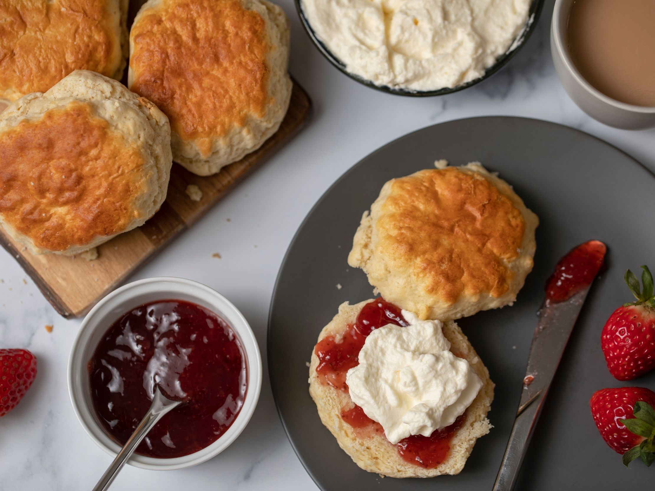 Freshly baked scones with strawberry jam and clotted cream on a plate with tea
