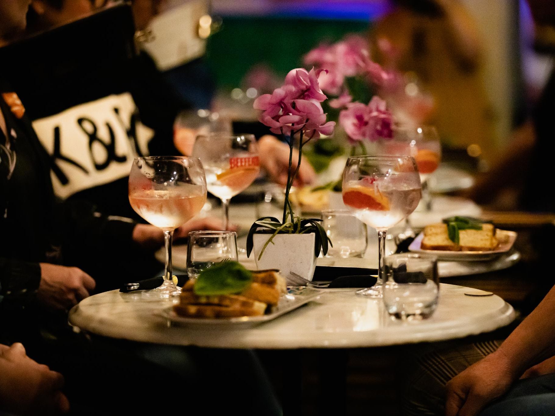 Cocktails and small plates on a restaurant table with pink flowers in the centre