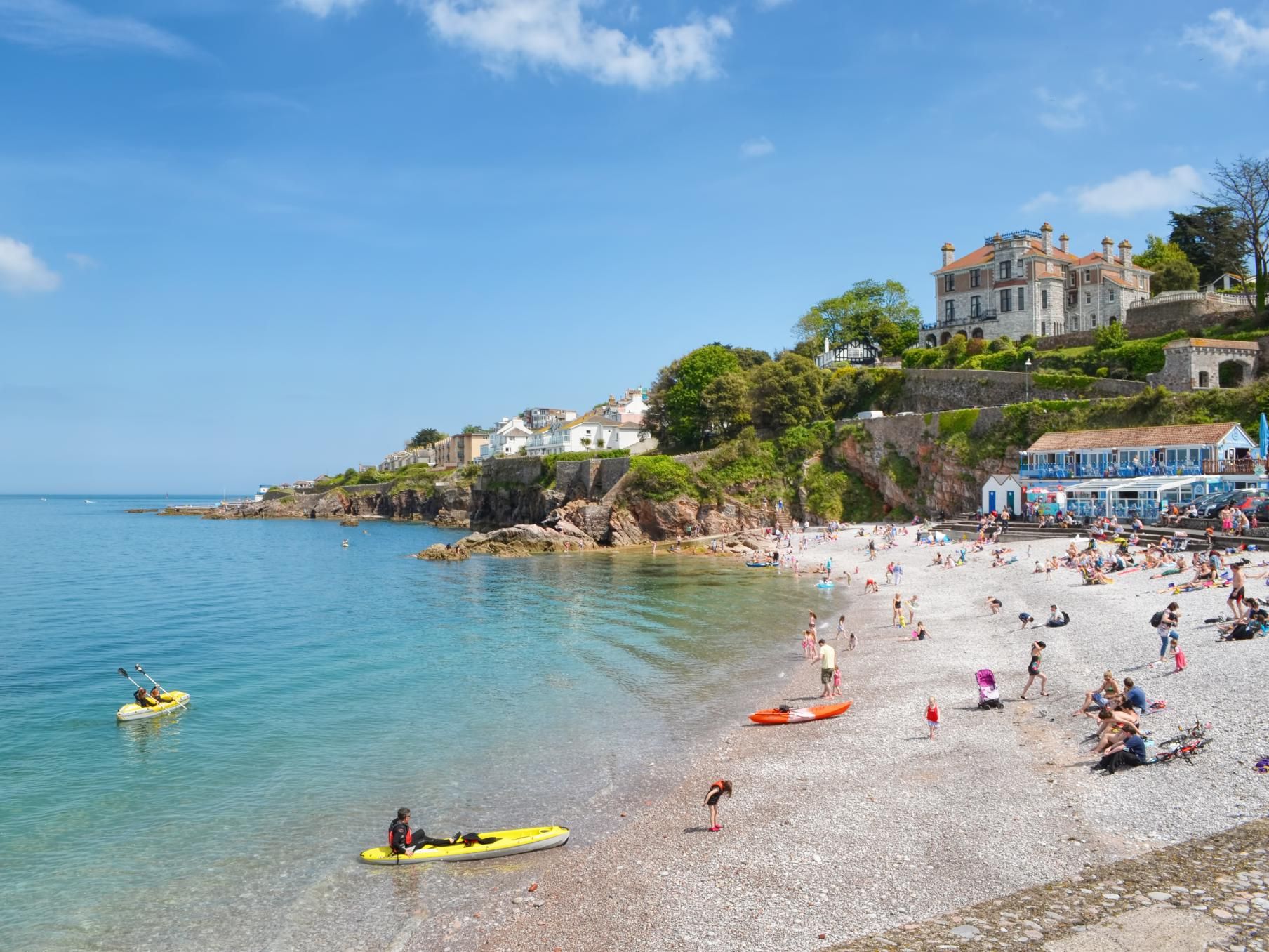 Pebble beach with kayakers and seaside houses on a sunny day