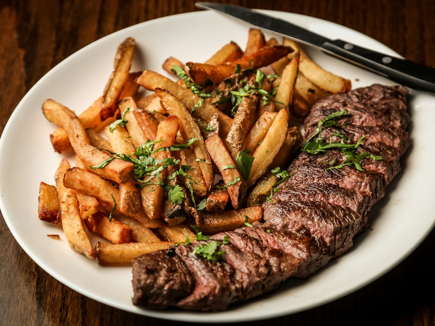 Plate of steak and chips with chopped herbs on a wooden table