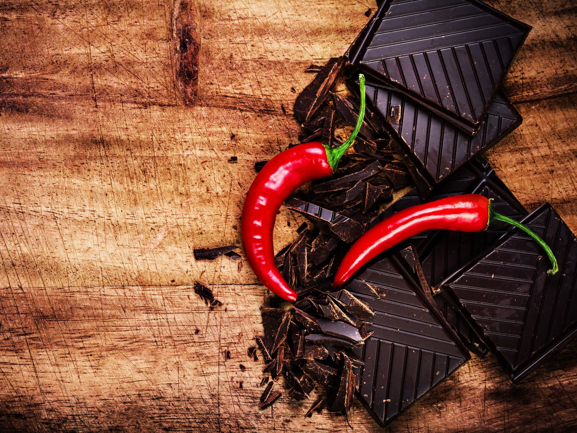 Dark chocolate pieces with two red chilli peppers on a rustic wooden surface