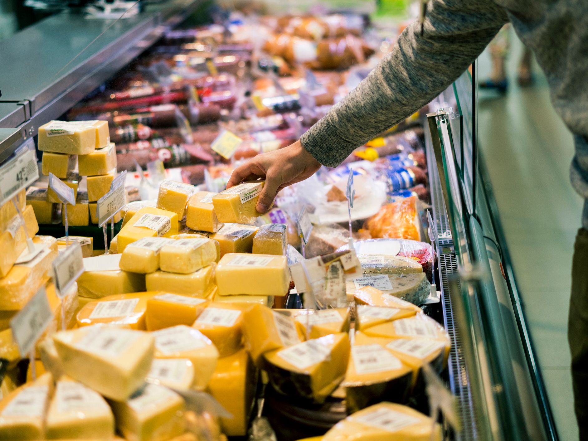 Shopper choosing a block of cheese from a supermarket deli counter