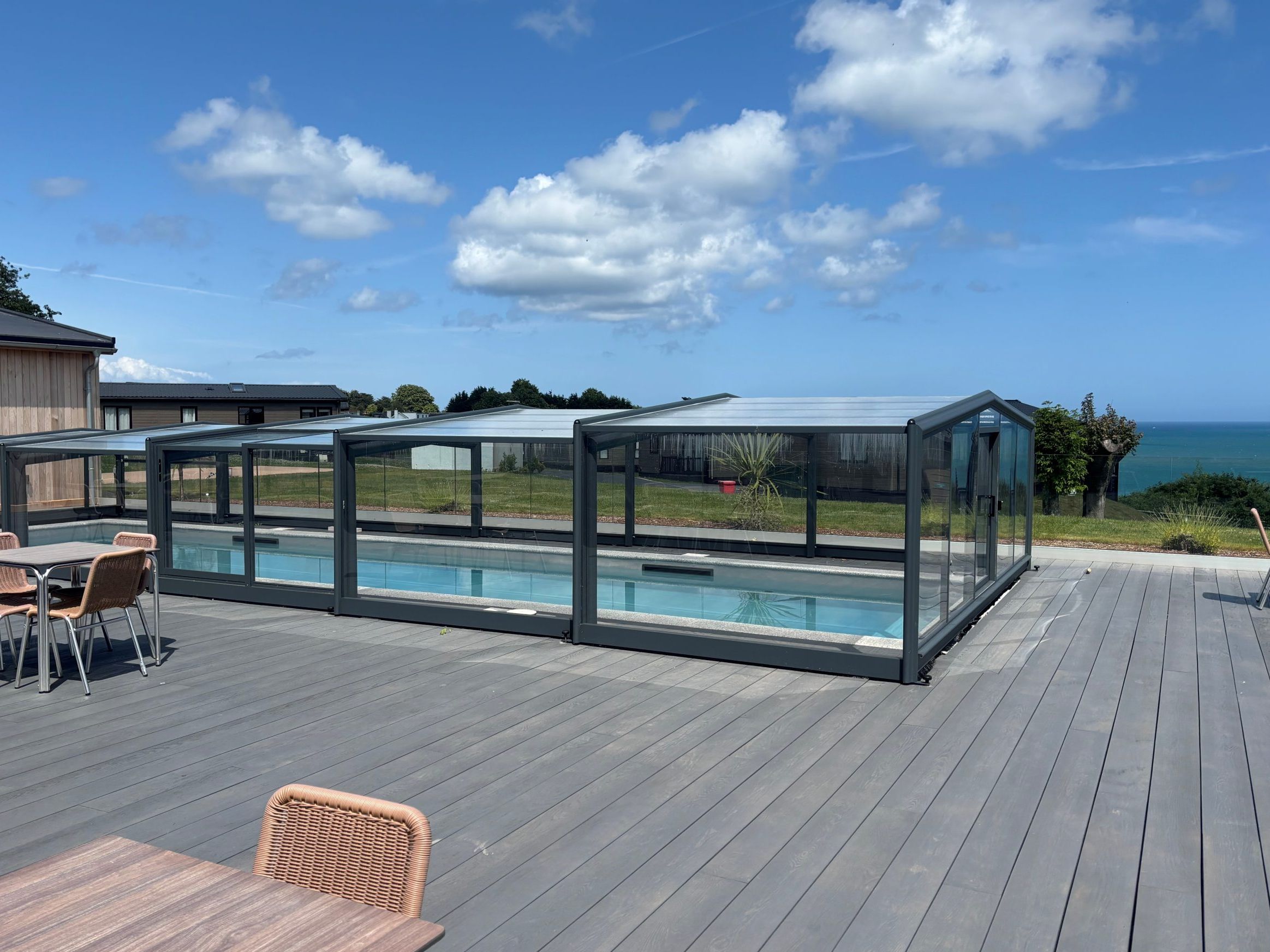 Outdoor swimming pool under a glass enclosure on a grey deck with sea view