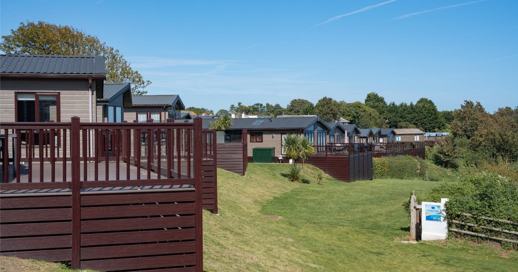 Row of holiday lodges with wooden decking on a grassy hillside under a clear blue sky