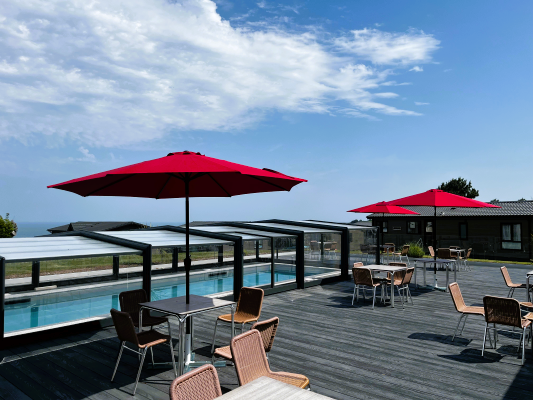 Outdoor terrace with red parasols, tables and chairs beside a covered swimming pool overlooking the sea