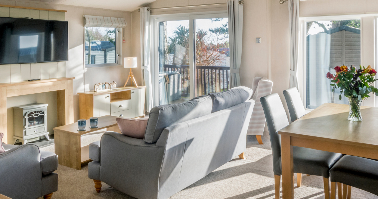 Bright lodge lounge with grey sofas, dining table, wall-mounted TV and sliding doors to a balcony