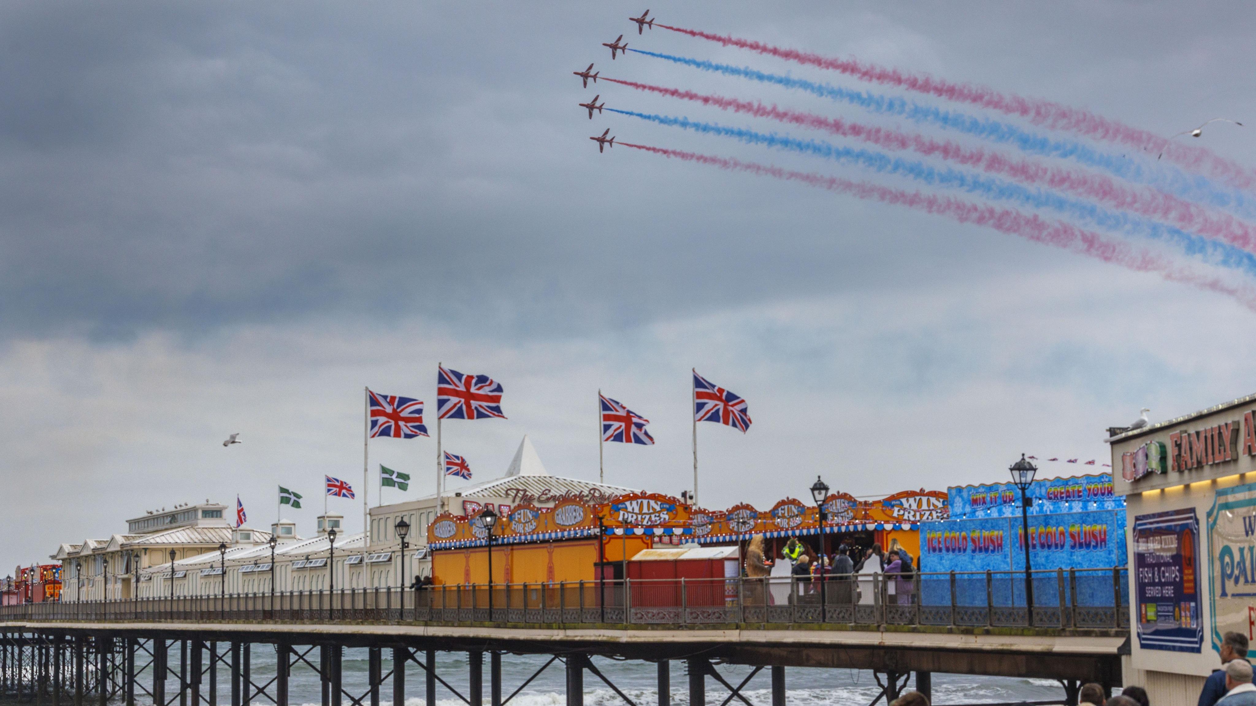 The Red Arrows fly in formation above Paignton Pier, leaving red, white and blue smoke trails as crowds watch below.
