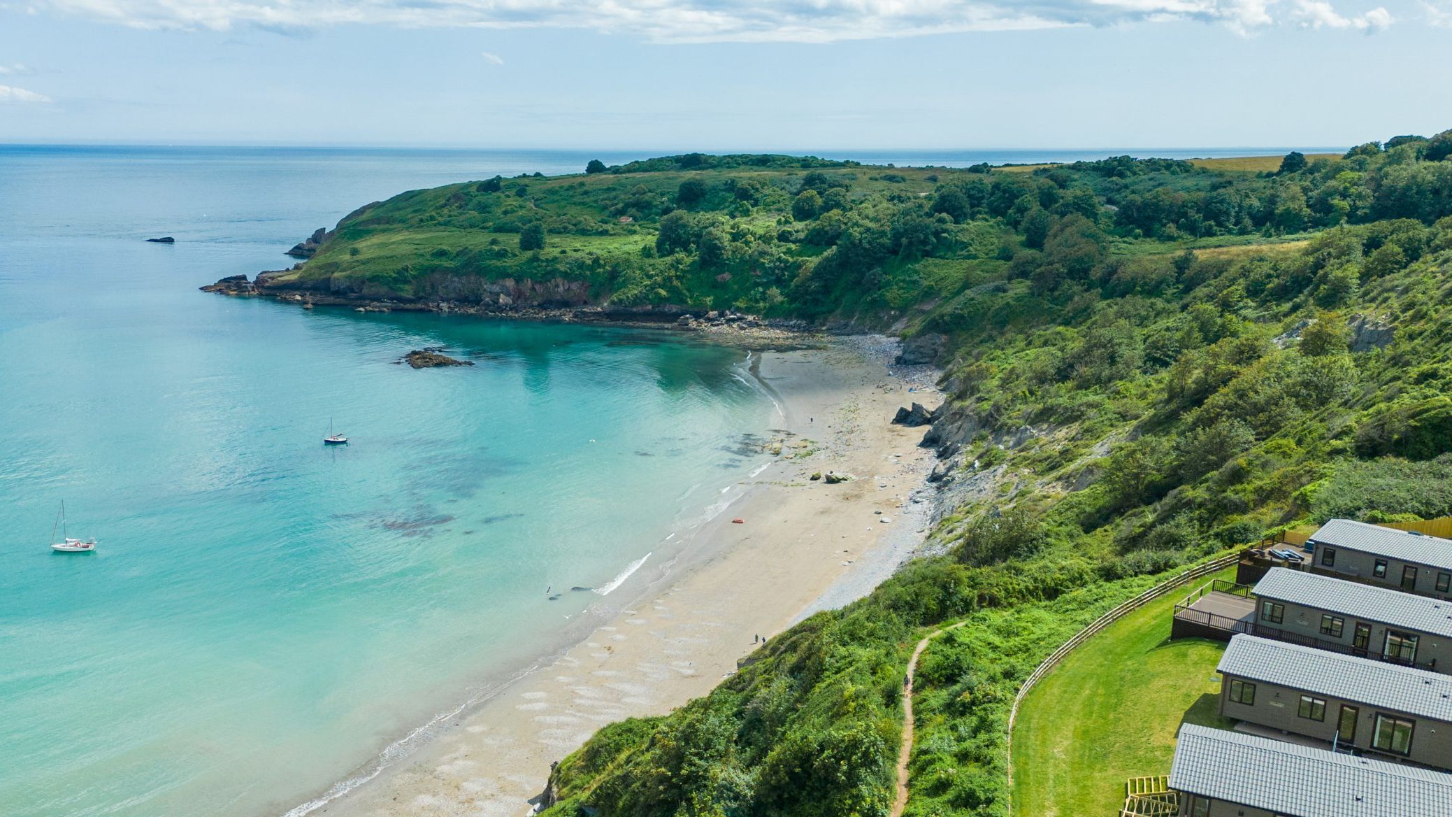 Drone view of a sandy bay with turquoise sea, green cliffs and coastal lodges