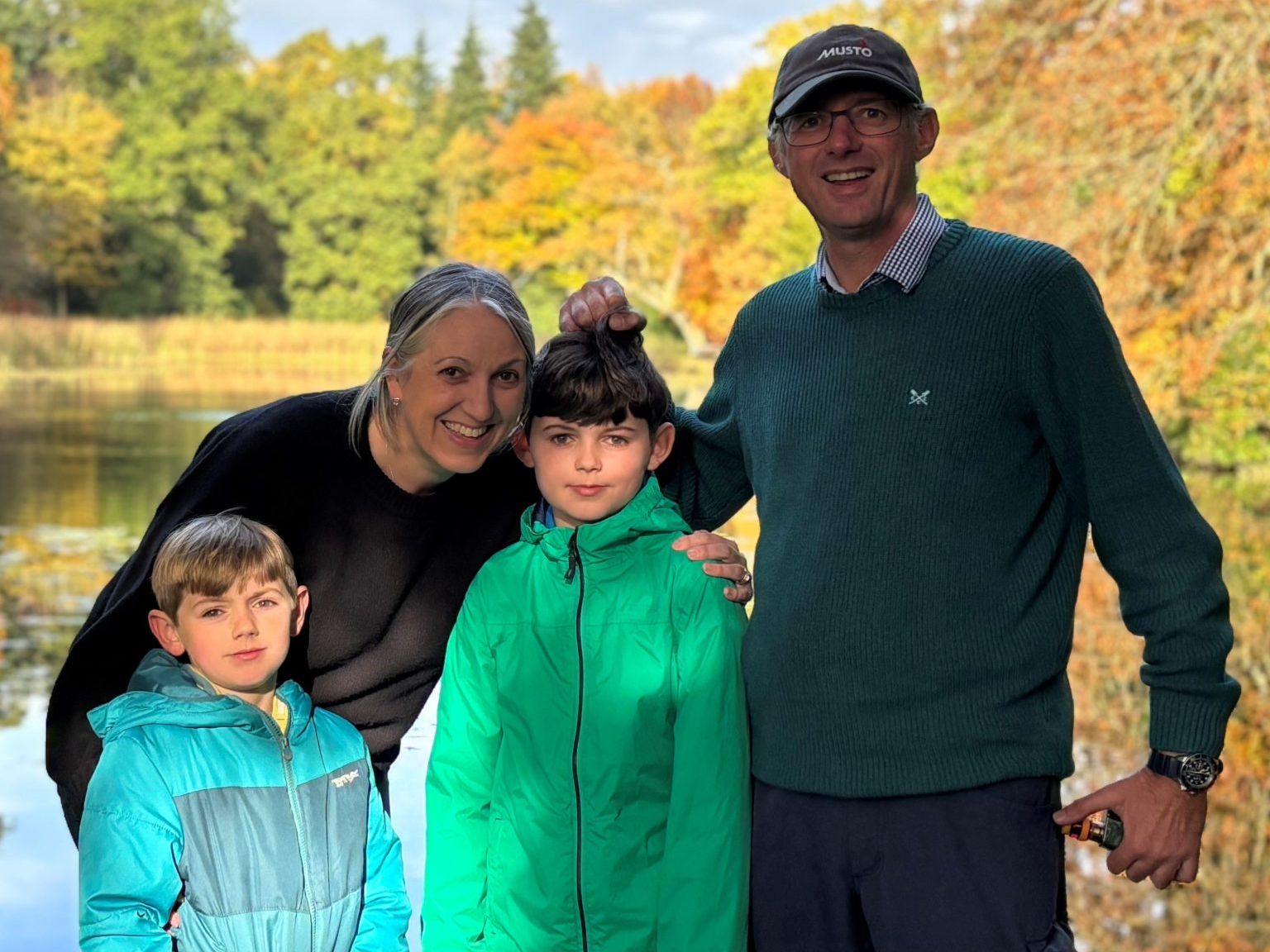 Family of four posing by a lake with autumn trees in the background