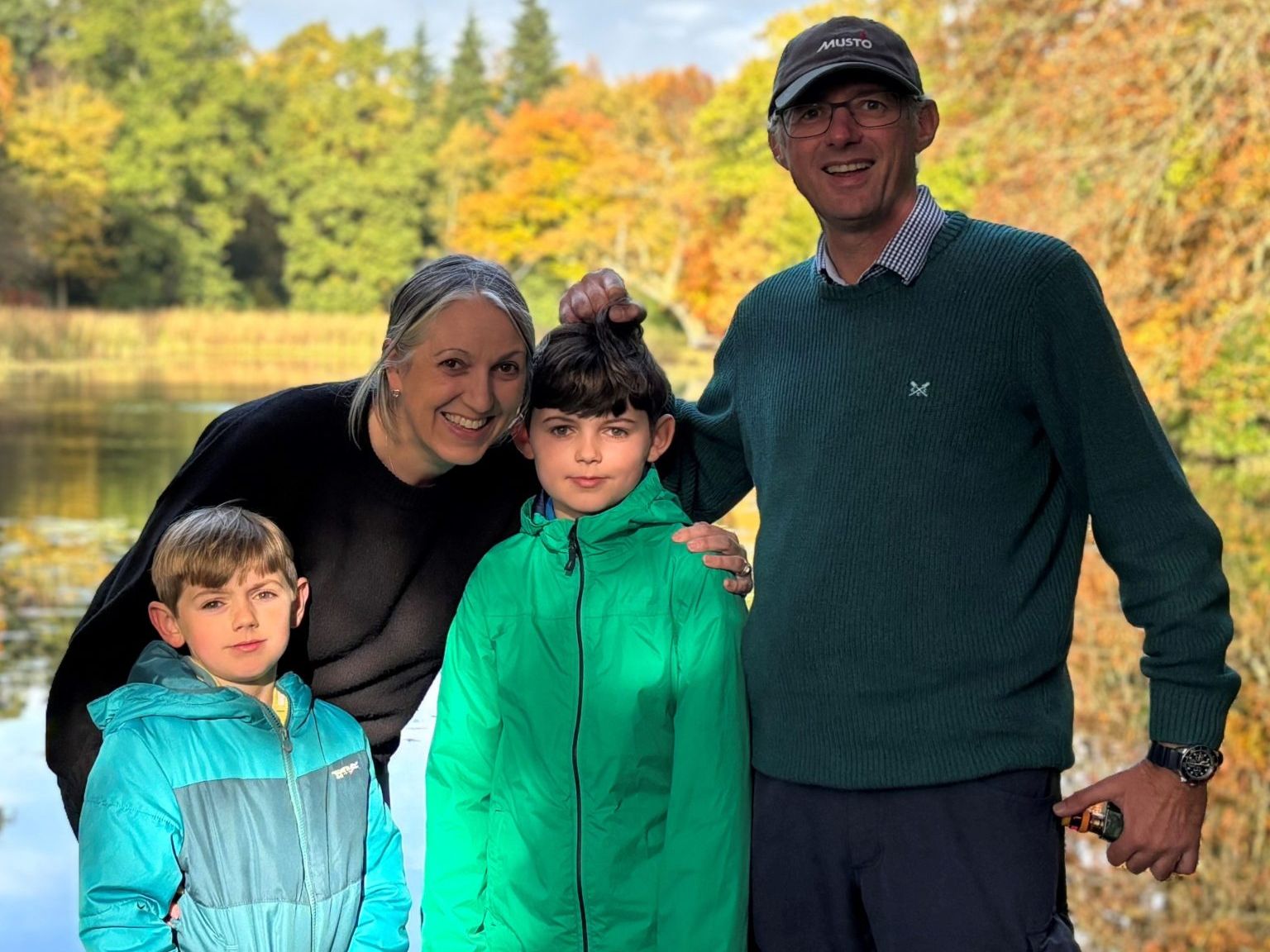 Family of four posing by a lake with autumn trees in the background