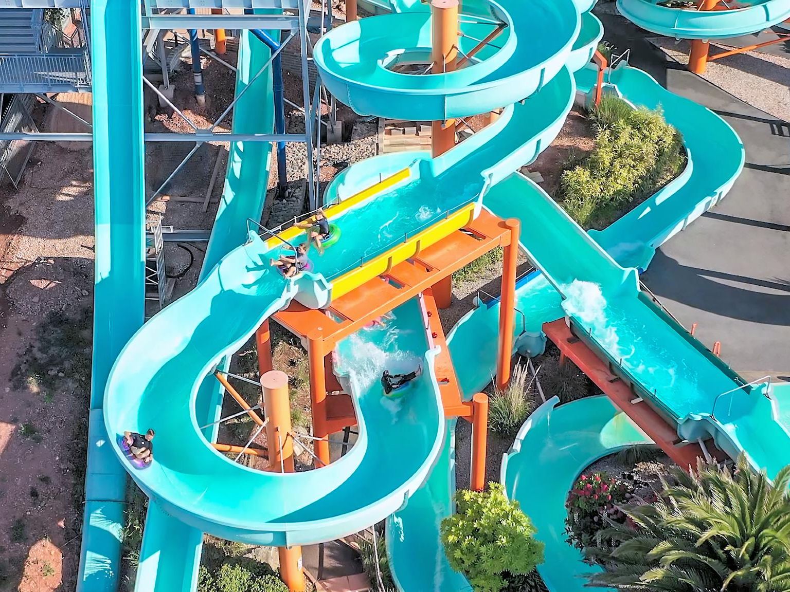 Aerial view of turquoise water slides at a water park with riders splashing through curves