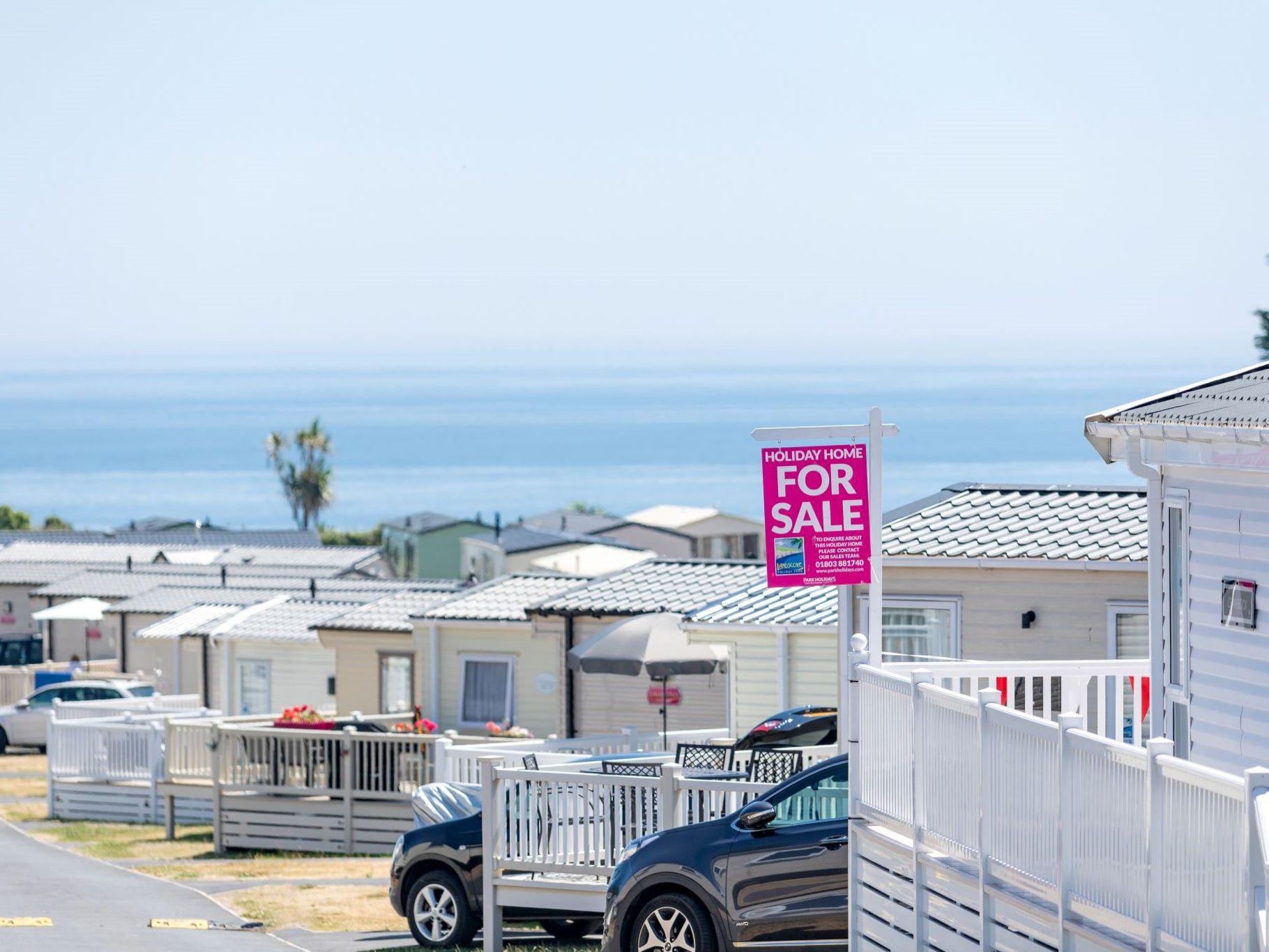 Static caravans at a coastal holiday park with sea view and a holiday home for sale sign