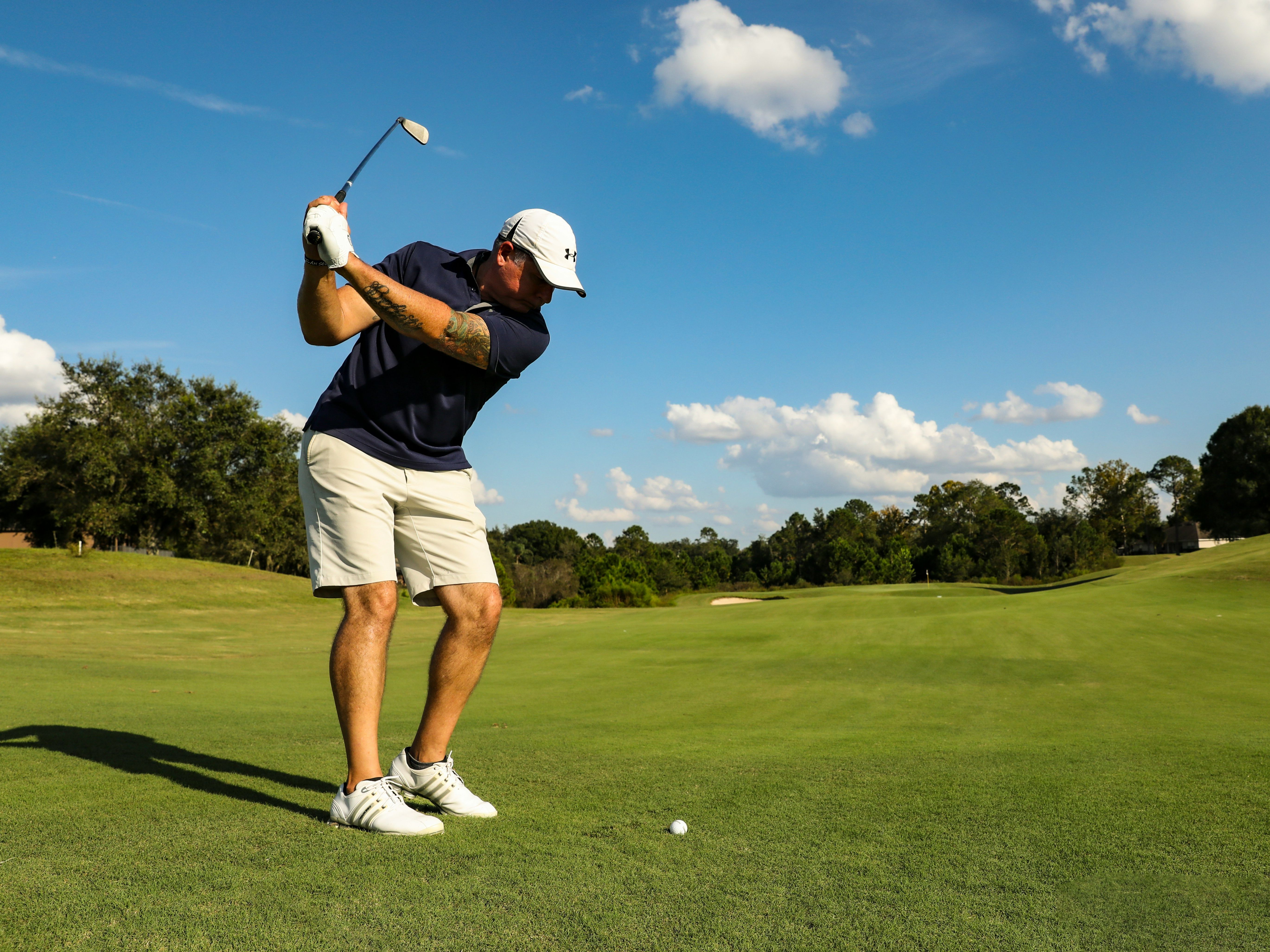 Golfer swinging an iron on a green fairway under a bright blue sky