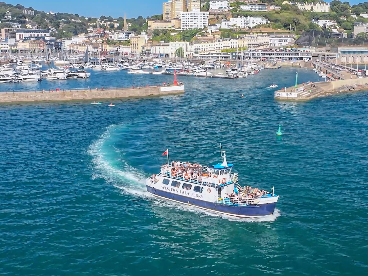 Passenger ferry leaving a marina harbour with a hillside town in the background