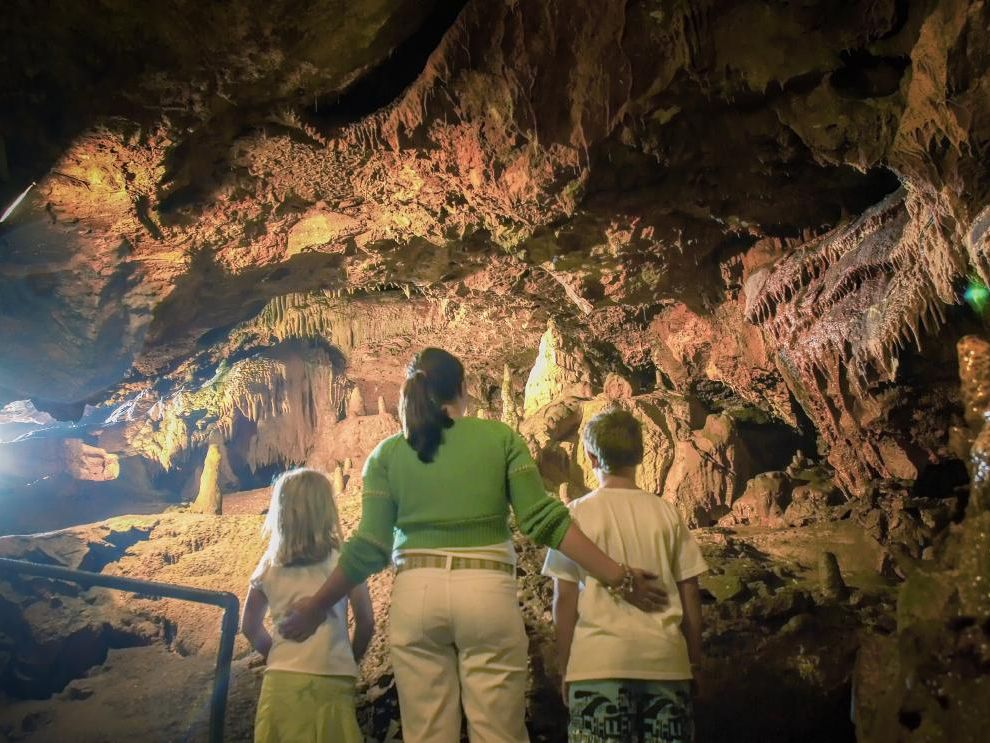 Adult and two children looking at stalactites and rock formations inside Kents Cavern