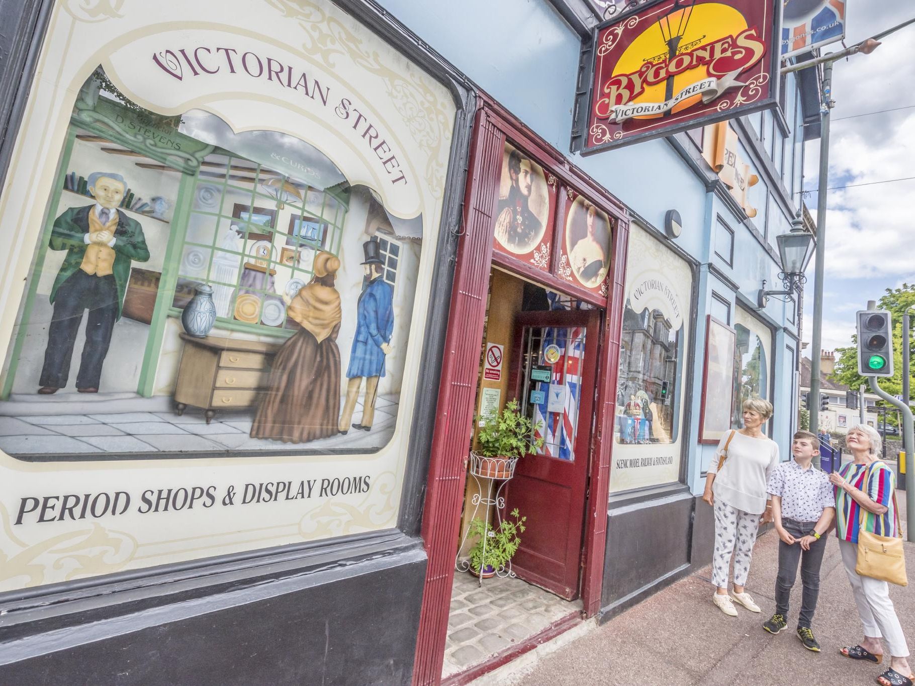 Visitors standing outside the Bygones Victorian Street entrance, with painted shopfront window displays and period signage