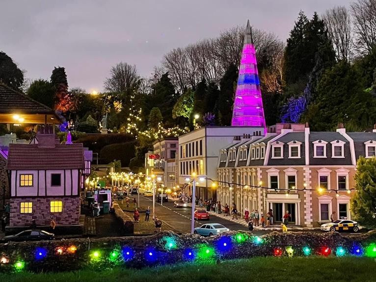 Miniature village street at dusk with Christmas lights and a glowing purple tower