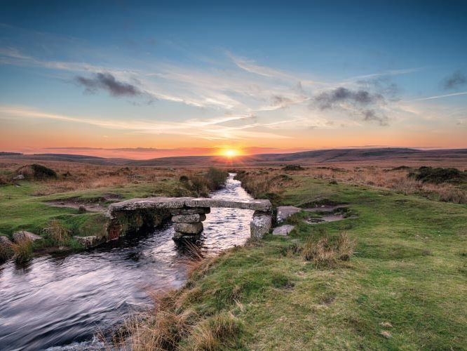 Sunrise over Dartmoor with a stone clapper bridge crossing a stream