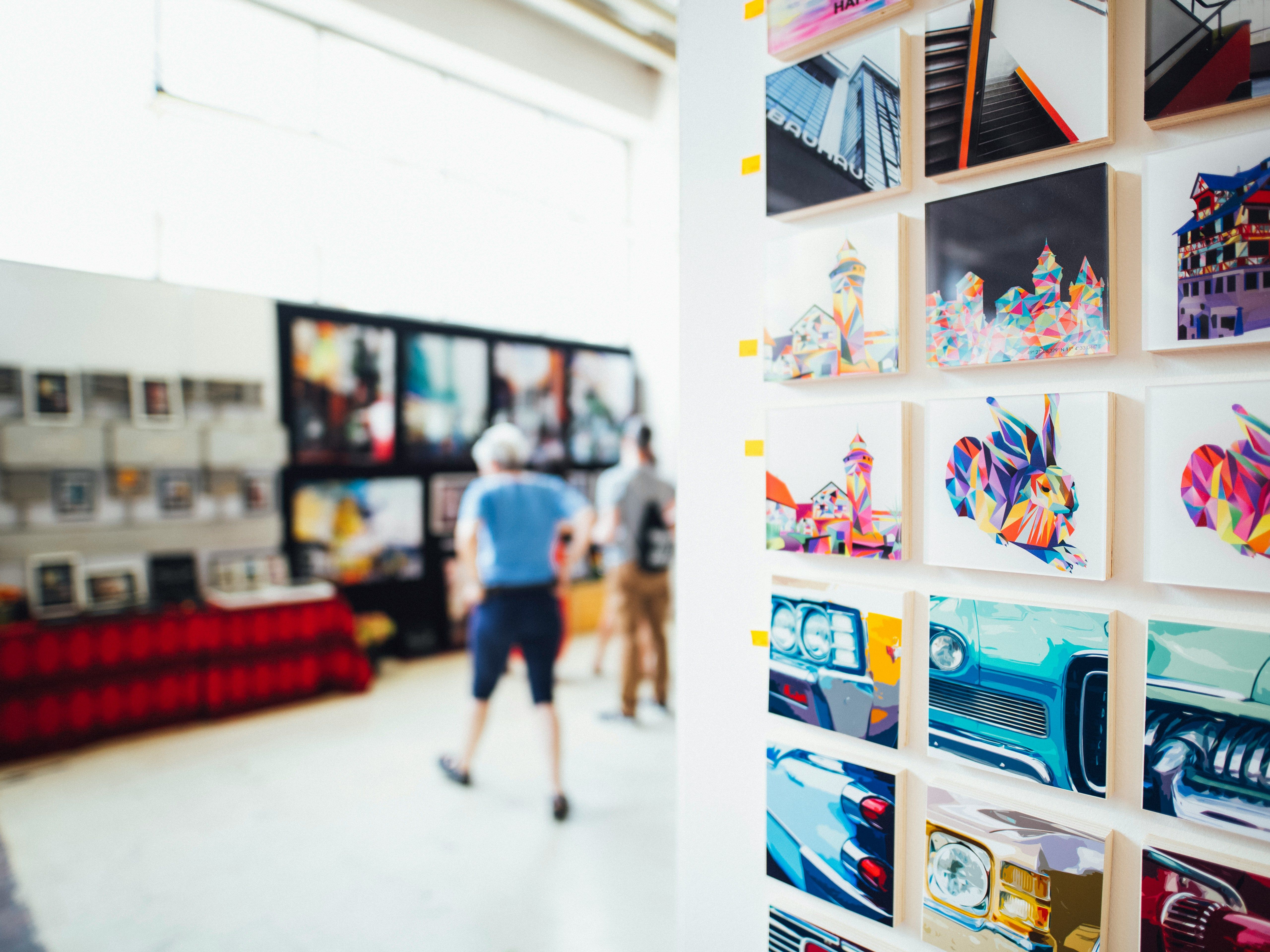 Wall of colourful modern art prints in a gallery with visitors in the background