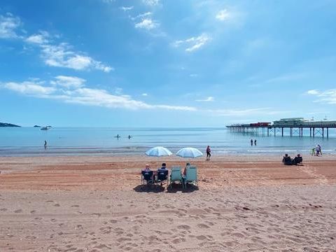 Sunny view of Paignton Sands with people relaxing on the beach, calm sea and a pier extending into the water