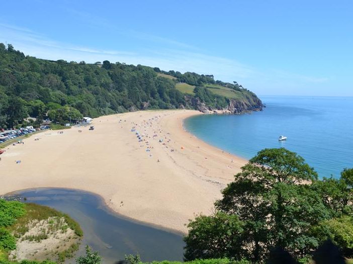Panoramic view of Blackpool Sands beach with golden sand, calm blue sea and green wooded cliffs