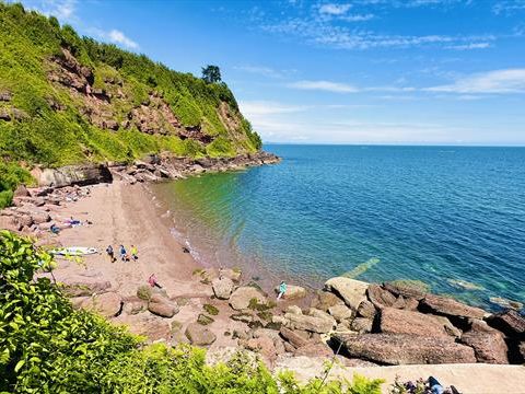 Maidencombe Beach with rocky shoreline, cliffside greenery and calm blue sea under a clear sky