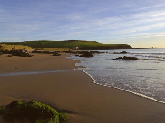 Sandy shoreline with gentle waves and rocky outcrops at Bantham Beach under a clear sky