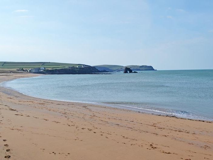 Wide sandy beach with calm sea, footprints in the sand and distant headland under a clear blue sky