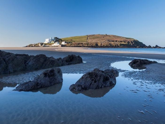 Rocky shoreline and tidal pools at Bigbury-on-Sea with Burgh Island in the distance under a clear blue sky
