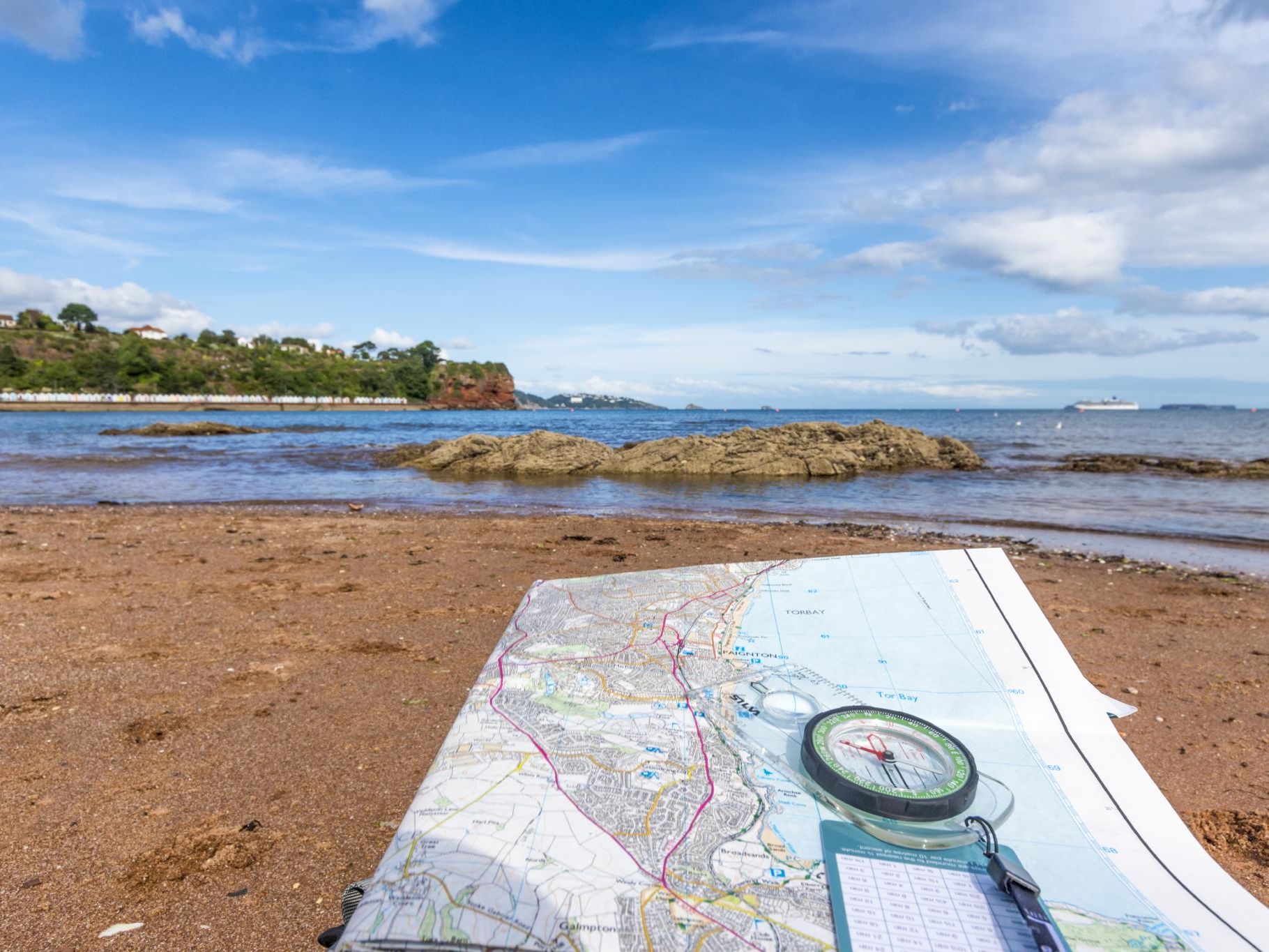 Ordnance Survey map and compass on a sandy beach beside the sea on the South West Coast Path