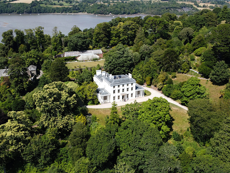 Aerial view of Greenway in South Devon, a large white mansion surrounded by lush greenery.