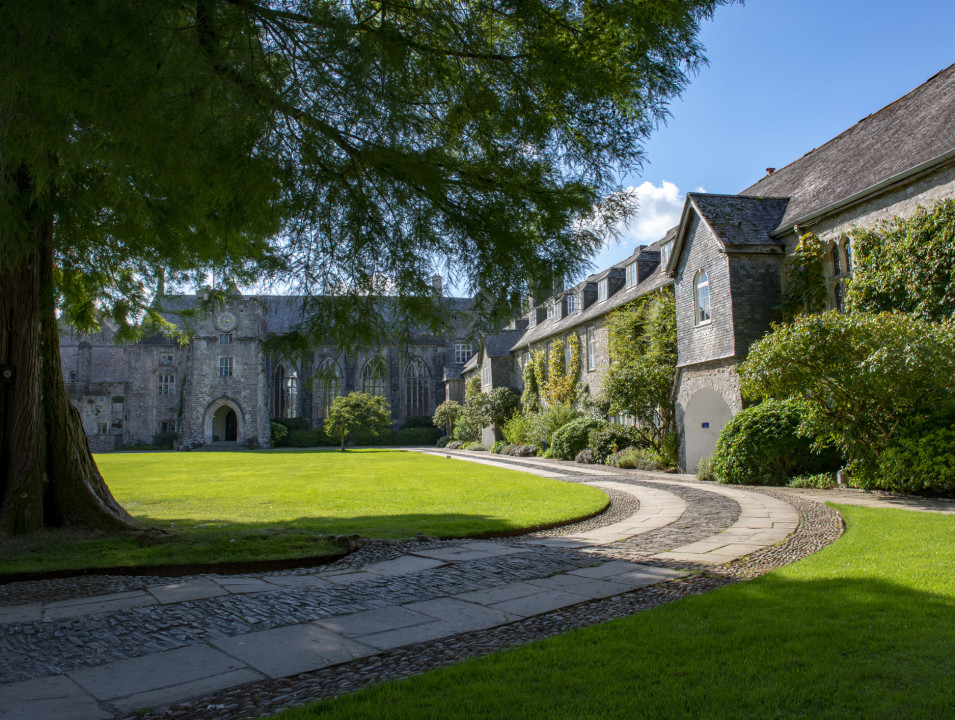 Dartington Hall building, feraturing arched windows, framed by a tree and lush green lawn.