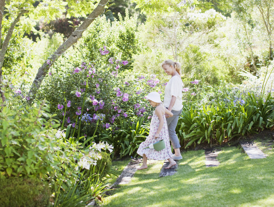 A woman and a child enjoying a peaceful stroll through a sunlit, flower-filled garden.