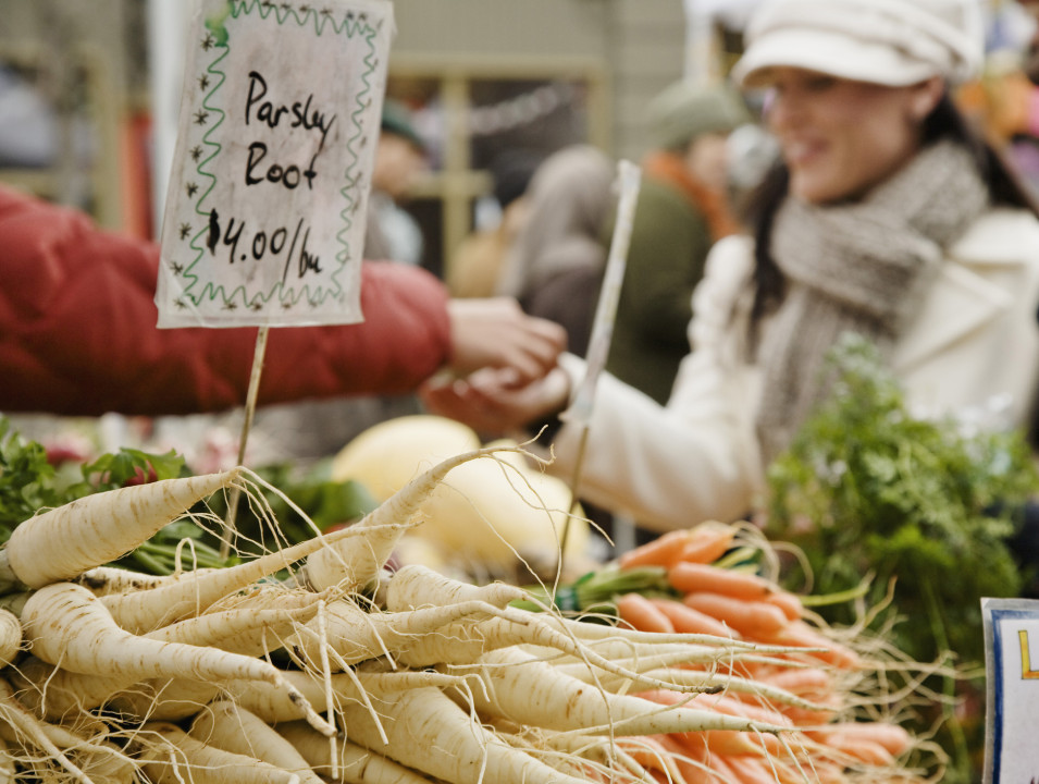 A pile of parsley roots at a farmer's market, with people shopping in the background.