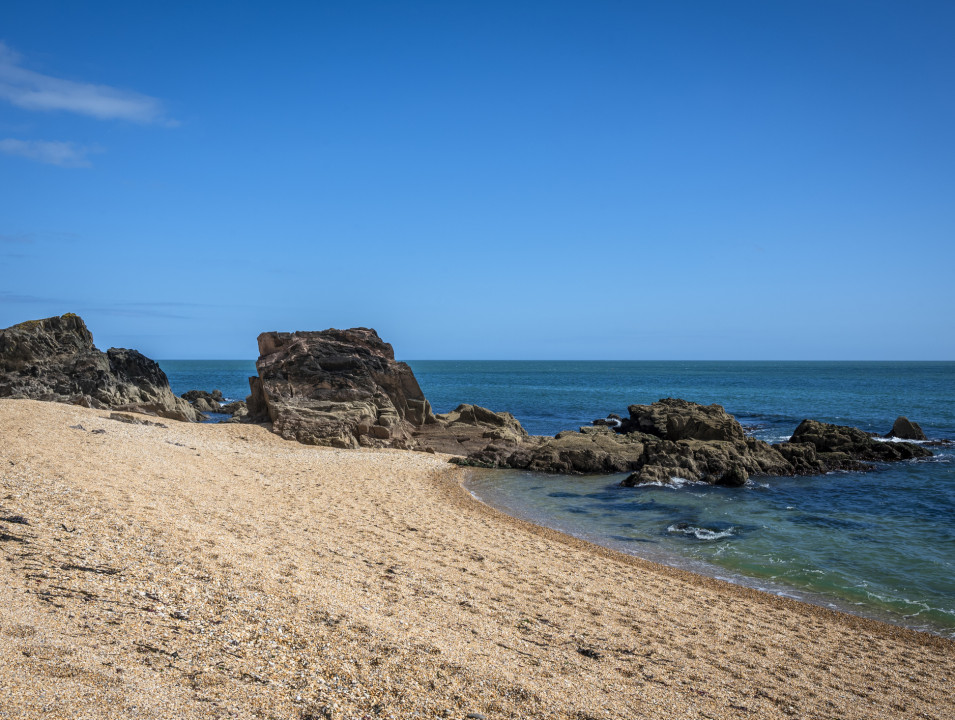 Rocky formations on a sandy beach, with clear blue waters stretching to the horizon.