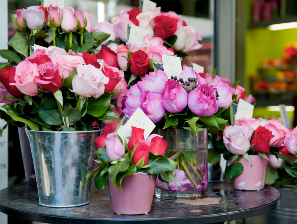 Bouquets of pink and red roses arranged in metal buckets and glass vases.