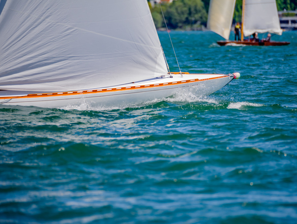 Close-up of a sleek white sailboat in motion, with another boat sailing nearby.