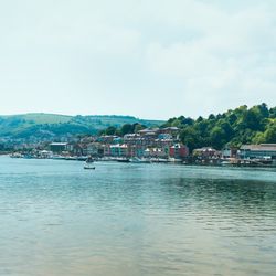 A scenic view of a riverside town with colorful buildings along the water, boats docked by the shore, and green hills in the background under a clear, bright sky.