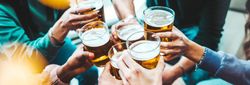 A group of friends raising glasses of beer in a cheerful toast, highlighting the social atmosphere often found in pubs in South Devon. The scene captures warmth and camaraderie.