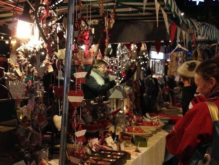 A festive evening scene at Christmas markets in Devon, featuring stalls decorated with twinkling lights and handmade crafts, as shoppers browse unique holiday gifts.
