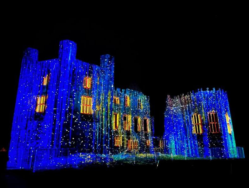 A historic building illuminated with vibrant blue and yellow lights, creating a magical ambiance during the festive season at Christmas markets in Devon.