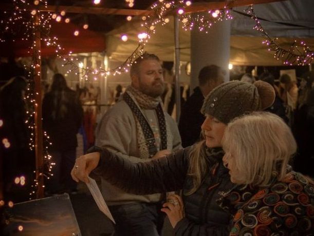Visitors browse under warm fairy lights at a cozy evening stall, enjoying the festive charm and unique offerings of Christmas markets in Devon.