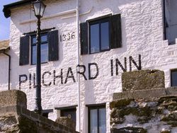 Pilchard Inn, one of the historic pubs in South Devon, featuring whitewashed stone walls, black shutters, and a vintage lamp post, exuding coastal charm and timeless appeal.