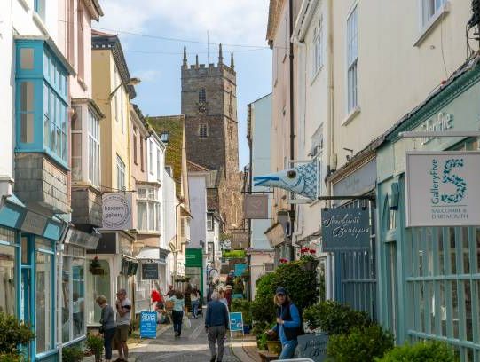Shops in historic buildings along alleyway with tower of church of St Saviour, Foss Street, Dartmouth, Devon, England, UK.