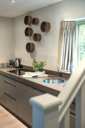 Modern kitchen with minimalist grey cabinets, wooden wall decor, countertop with a kettle, toaster, potted plant, and a window with curtains.