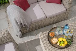Wicker patio furniture with a cozy throw blanket, red cushions, and a tray with drinks, lemons, and snacks.