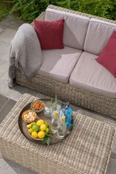 Outdoor wicker sofa and table with drinks, lemons, snacks, and red pillows